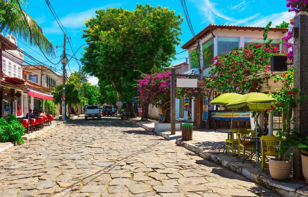 Rua das Pedras em dia de sol, com calçamento de pedra portuguesa, buganvílias floridas e mesas de bar nas calçadas.